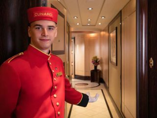 Bellboy standing in entrance to state room onboard a Cunard cruise ship - Accent On Travel